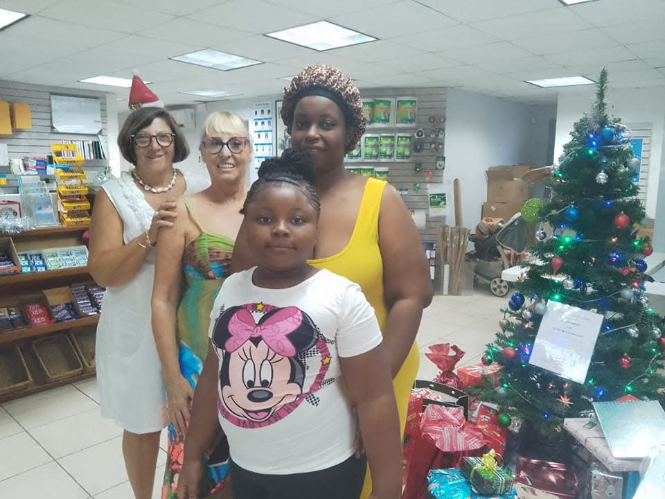 A child and three adults posing together beside a decorated Christmas tree and presents